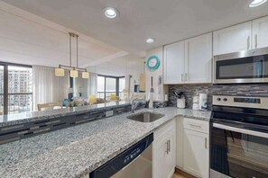A modern kitchen with granite countertops, stainless steel appliances, and white cabinetry. - Bright, ocean-view condo with balcony, AC, pools, saunas & gym (Ocean City)