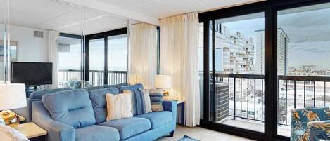 A modern living room with a sofa, a TV, and a balcony with a city view.