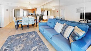 Una sala de estar moderna con un sofá azul, un comedor con una mesa y sillas, y una cocina al fondo.