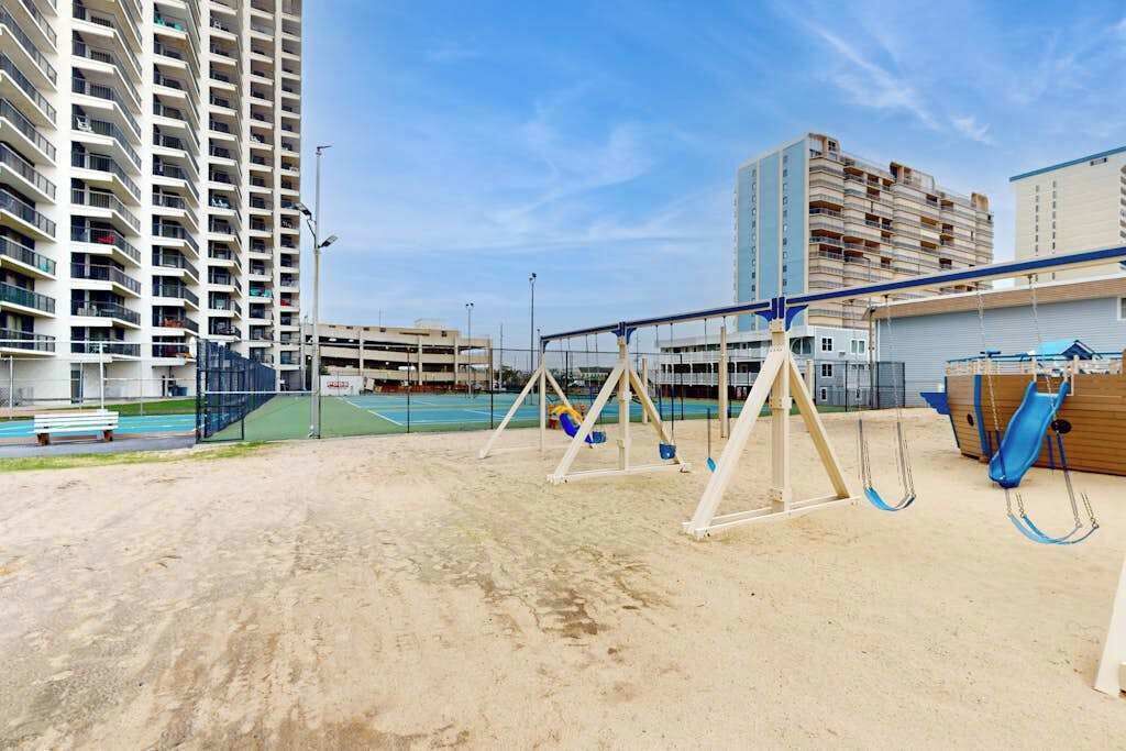 A sandy outdoor area with swings and a basketball court, surrounded by high-rise buildings.