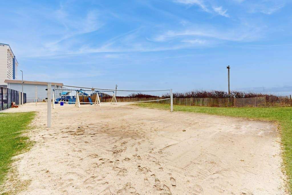 Un terrain de volleyball extérieur, équipé d’un filet, entouré d’une zone sablonneuse et d’un terrain herbeux.
