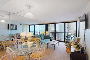 A modern living room with a sofa, chairs, a coffee table, and a TV. - Ocean-view condo with balcony, AC, pools, tennis, saunas & gym (Ocean City)