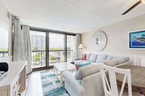 Un salon moderne avec un canapé, une table basse et une table à manger. Une grande fenêtre offre une vue sur les bâtiments environnants.