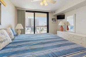 A hotel room with a large bed, a balcony with a view, a TV, and a dresser. - Well-located & equipped beach condo with pools, gym, sauna & central AC (Ocean City)