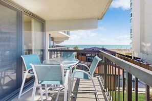 A balcony with a table and chairs, overlooking a beach and a hotel building. - Well-located & equipped beach condo with pools, gym, sauna & central AC (Ocean City)