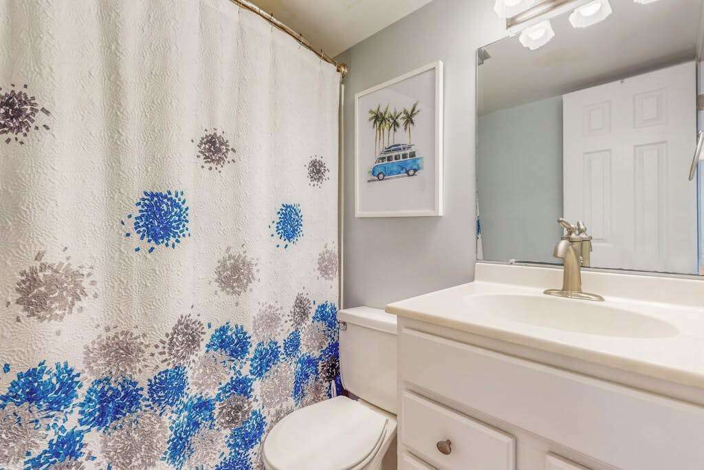 Un baño con cortina de ducha, inodoro, lavabo con espejo y un cuadro en la pared.