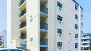 A multi-story building with balconies, a sign indicating 'El Sano,' and a clear sky.