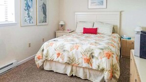 A bedroom with a bed, a nightstand, a lamp, and framed artwork on the wall.
