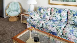 A living room with a floral sofa, a wicker chair, a glass coffee table, and a lamp.