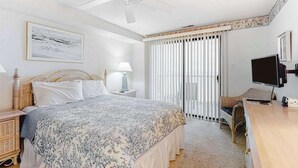 A bedroom with a bed, a desk, a chair, a television, a ceiling fan, and a window with blinds. - Sandy Square 404 (Ocean City)