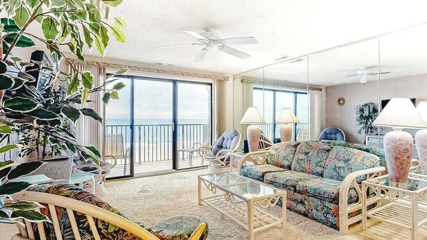 A spacious living room with a large sofa, a coffee table, and a chair. There is a balcony with a view, and the room has a ceiling fan. - Sandy Square 404 (Ocean City)