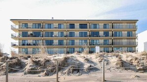 A multi-story hotel with balconies, situated on a sandy beach with dunes in the foreground. - Sandy Square 404 (Ocean City)