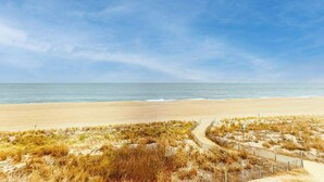 A beach with a sandy path leading to the water, surrounded by grassy dunes. - Sandy Square 404 (Ocean City)