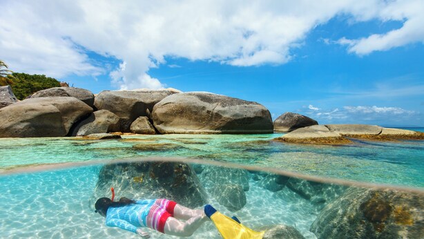 A person snorkeling in clear water with large rocks and a clear sky.