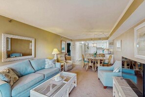 A living room with a sofa, coffee table, and dining area with chairs. - Sandpiper Dunes 302 (Ocean City)