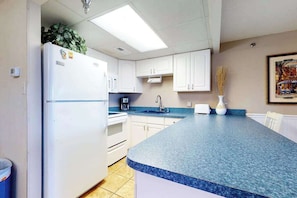 A kitchen with white cabinets, a blue countertop, a refrigerator, a coffee maker, and a sink. - Oceanfront, Ground-Floor Condo w/ Patio, Fast WiFi, Central AC & Washer/Dryer (Ocean City)