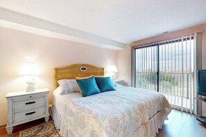 A bedroom with a bed, two bedside tables, a TV, and a window with blinds. - Oceanfront, Ground-Floor Condo w/ Patio, Fast WiFi, Central AC & Washer/Dryer (Ocean City)