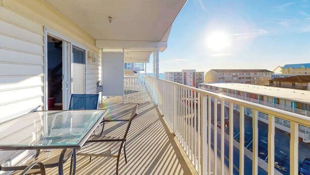 Ein Balkon mit Glastisch und Stühlen, der auf einen Parkplatz und Gebäude blickt.