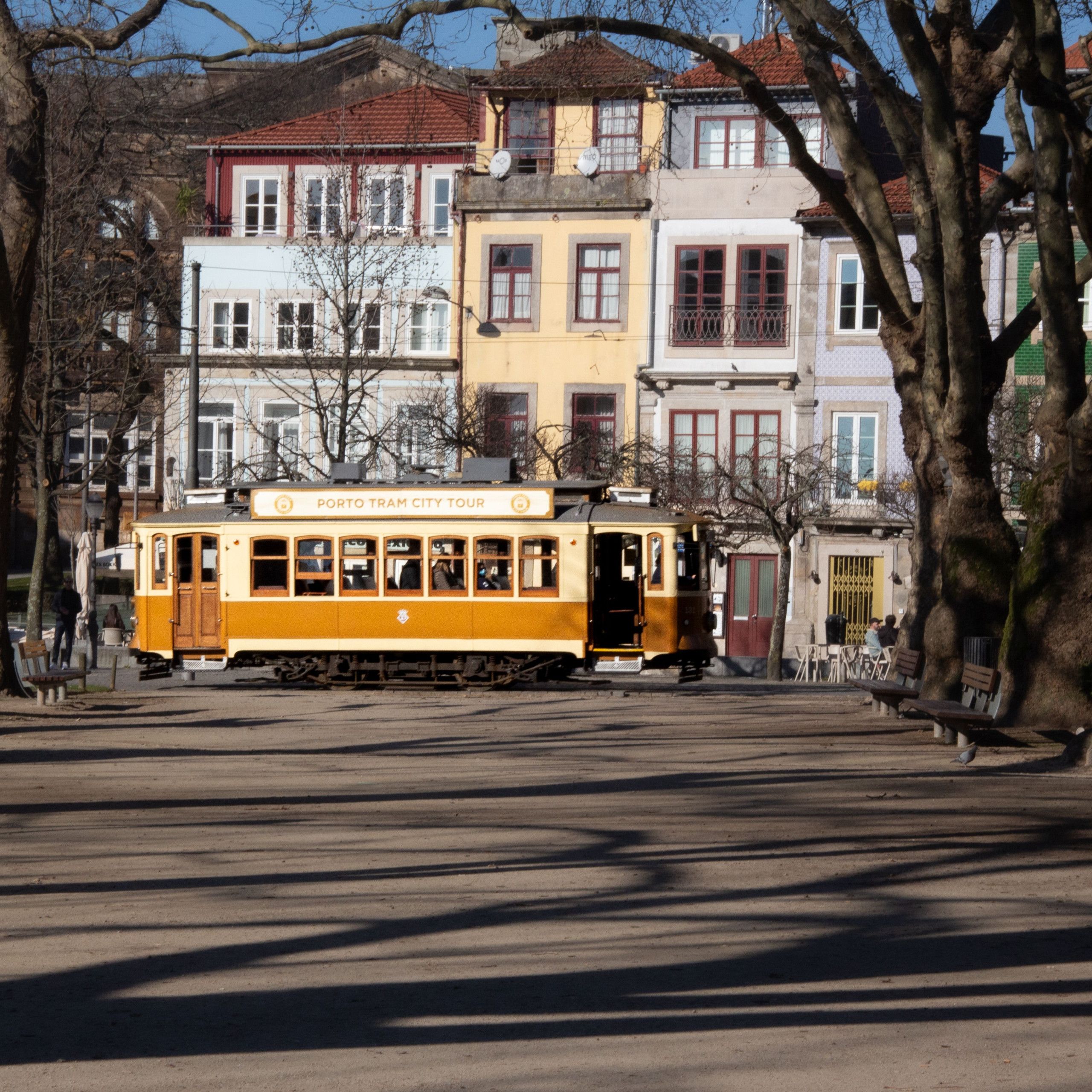 Eine gelbe Straßenbahn mit der Aufschrift 'PORTO TRAM CITY TOUR', geparkt auf einer Gleisstrecke, Gebäude im Hintergrund.