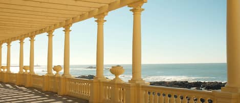 A covered walkway with columns and balustrades overlooking the ocean.