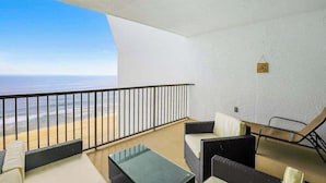 A balcony with a view of the ocean, a glass table, and two black wicker sofas. - Oceanfront condo with ocean view, private W/D, central AC, and pool access (Ocean City)