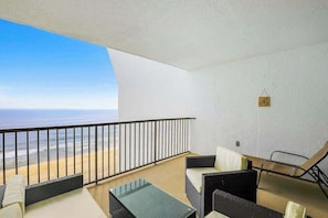 A balcony with a view of the ocean, a glass table, and two black wicker sofas. - Oceanfront condo with ocean view, private W/D, central AC, and pool access (Ocean City)