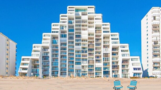 A multi-story hotel with a modern architectural design, featuring balconies and a beachside location. - Oceanfront condo with ocean view, private W/D, central AC, and pool access (Ocean City)