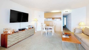 A modern living room with a flat-screen TV, a dining area with white chairs, a sofa, and a coffee table. - Oceanfront condo with ocean view, private W/D, central AC, and pool access (Ocean City)