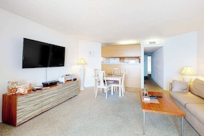 A modern living room with a flat-screen TV, a dining area with white chairs, a sofa, and a coffee table. - Oceanfront condo with ocean view, private W/D, central AC, and pool access (Ocean City)