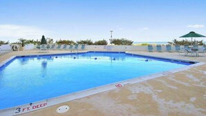 A swimming pool with lounge chairs and umbrellas, surrounded by greenery. - Oceanfront condo with ocean view, private W/D, central AC, and pool access (Ocean City)