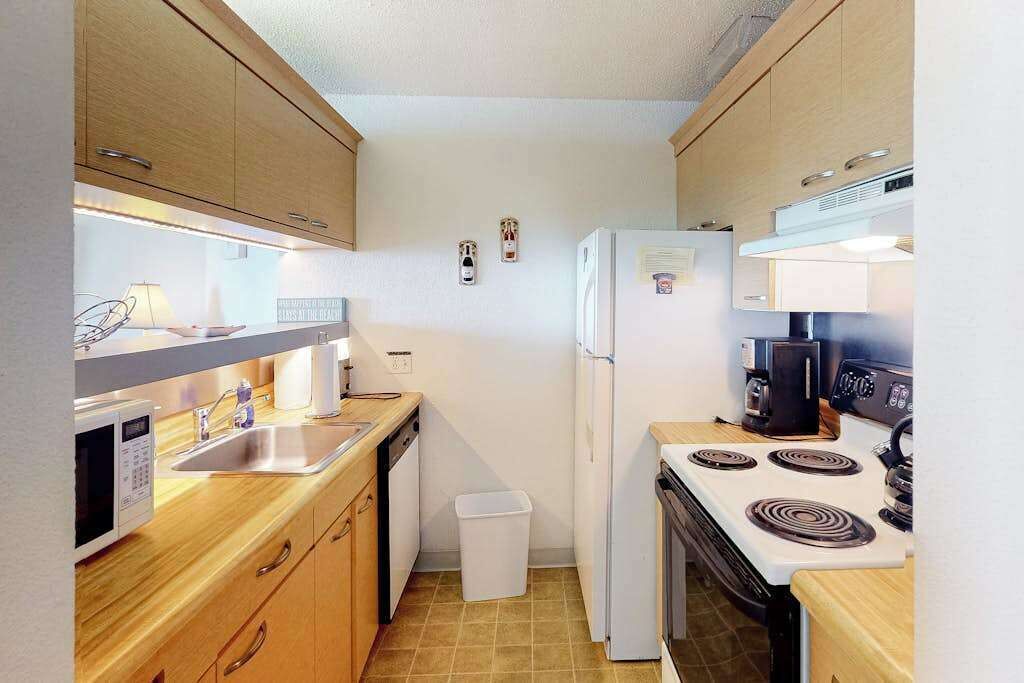 Une cuisine de taille réduite, dotée de meubles en bois, d’un four à micro-ondes, d’un évier, d’un réfrigérateur et d’une cuisinière.