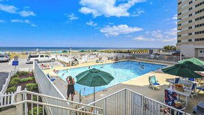 A rooftop pool with a view of the ocean, lounge chairs, and umbrellas. - Ideal waterfront condo with pools, private balcony & W/D (Ocean City)