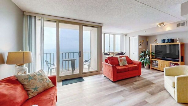 A spacious living area with a red sofa, a yellow armchair, a television, and a balcony with a table and chairs. - Ideal waterfront condo with pools, private balcony & W/D (Ocean City)