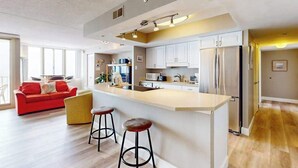A modern kitchen with a central island, bar stools, and a red sofa in the living area. - Ideal waterfront condo with pools, private balcony & W/D (Ocean City)