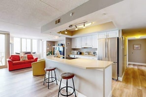A modern kitchen with a central island, bar stools, and a red sofa in the living area. - Ideal waterfront condo with pools, private balcony & W/D (Ocean City)
