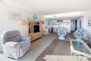 Ein Wohnzimmer mit einer Couch, einem Glastisch, einem Fernseher und einem Essbereich mit Stühlen.