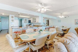 Una cocina amplia con armarios blancos, un comedor con sillas blancas y un ventilador de techo.
