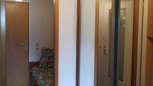 A room with a bed, a wooden door, a mirror, and a ceiling light fixture.
