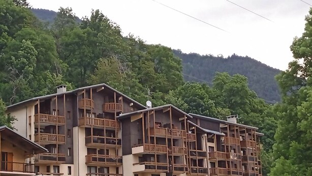 A multi-story building with balconies, surrounded by greenery and hills.