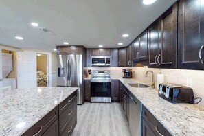 A modern kitchen with stainless steel appliances, dark cabinetry, and a granite countertop. - Plaza 211 (Ocean City)