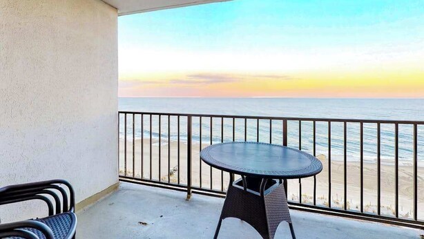 A balcony with a table and chairs, overlooking a beach and ocean during sunset. - Plaza 1109 (Ocean City)