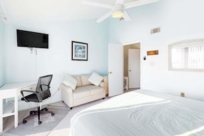 A bedroom with a bed, a desk with a chair, a sofa, a television, and a door leading to another room. - Two-Level Bayfront Condo with Amazing Sunsets, Balcony, WiFi & Shared Pool (Ocean City)