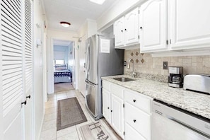 A kitchen with white cabinets, stainless steel appliances, and a granite countertop. - Two-Level Bayfront Condo with Amazing Sunsets, Balcony, WiFi & Shared Pool (Ocean City)