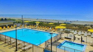 Área da piscina com vários espreguiçadeiras e guarda-sóis, vista desobstruída da praia e piscina cercada.