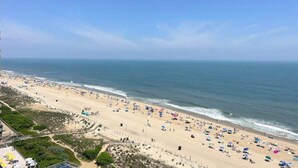 Uma praia com guarda-sóis e pessoas, céu claro e vista para o oceano.