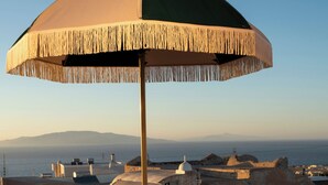 Eine Dachterrasse mit zwei Liegestühlen, einem Tisch mit Getränken und einem großen Sonnenschirm.