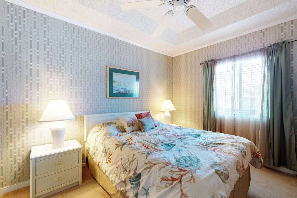 A bedroom with a bed, two bedside lamps, a nightstand, a framed picture on the wall, and a window with curtains.