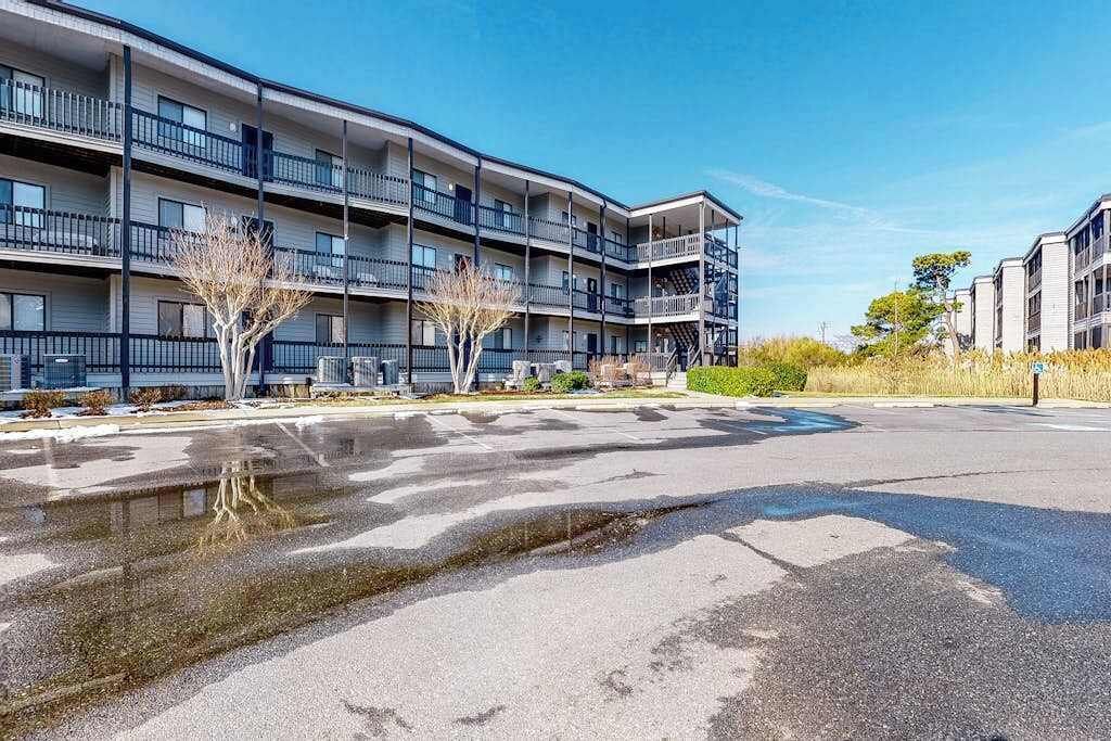 A multi-story residential building with balconies, a parking lot, and a small tree.