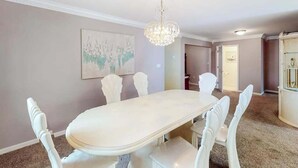 Un coin repas avec une table et des chaises blanches, un lustre et un tableau au mur.
