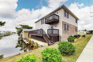 A two-story house with a dock extending into a body of water, surrounded by greenery. - Multi-Level Home Close to the Beach w/Air Hockey, Free WiFi, Decks, & Balconies (Ocean City)